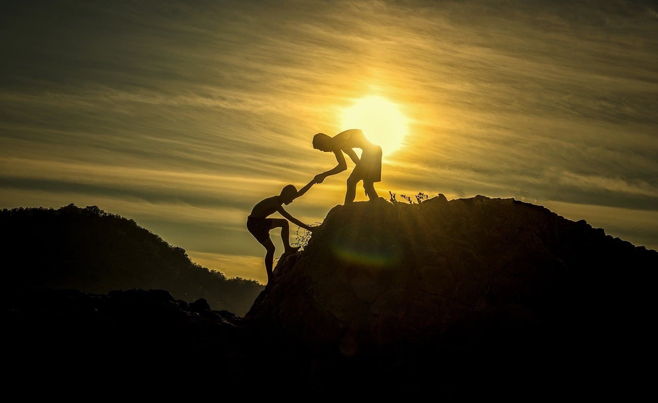 one person helping another up a mountain